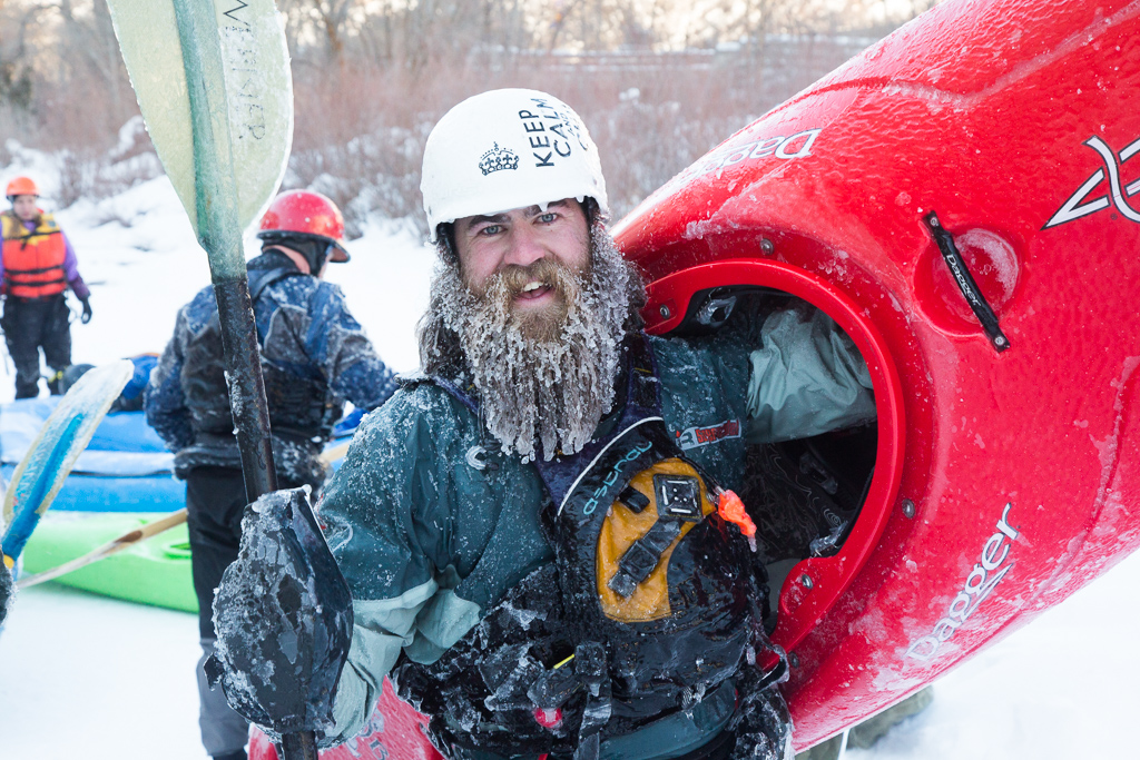 Man with a frozen beard holding up his kayak.