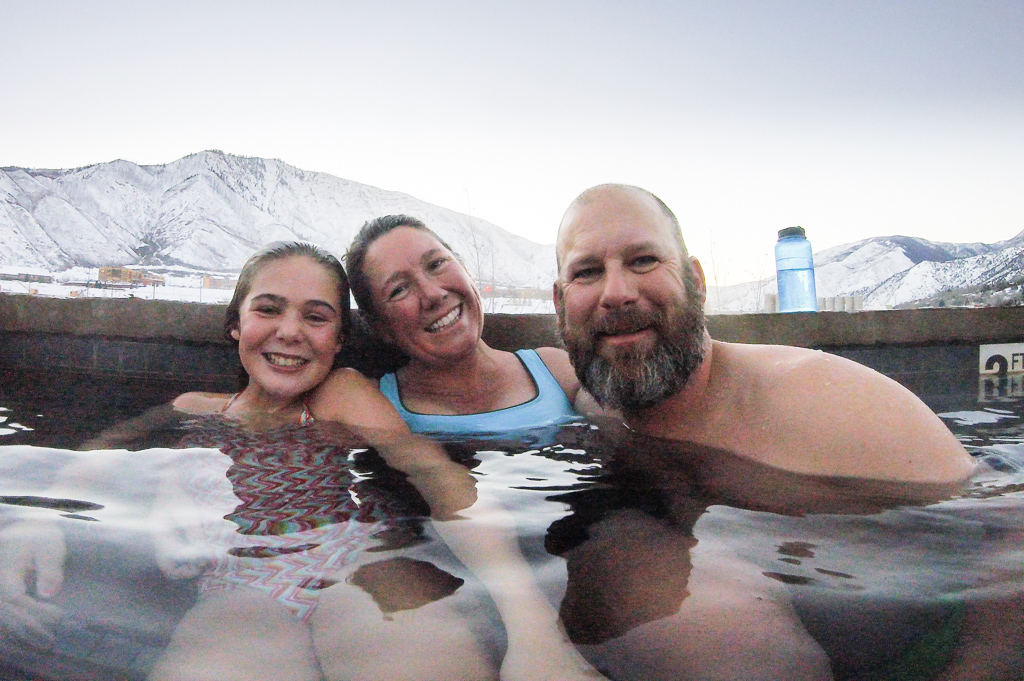 Peter, Abby, and Kathy Holcombe in a hot tub with snow covered mountains in the background.
