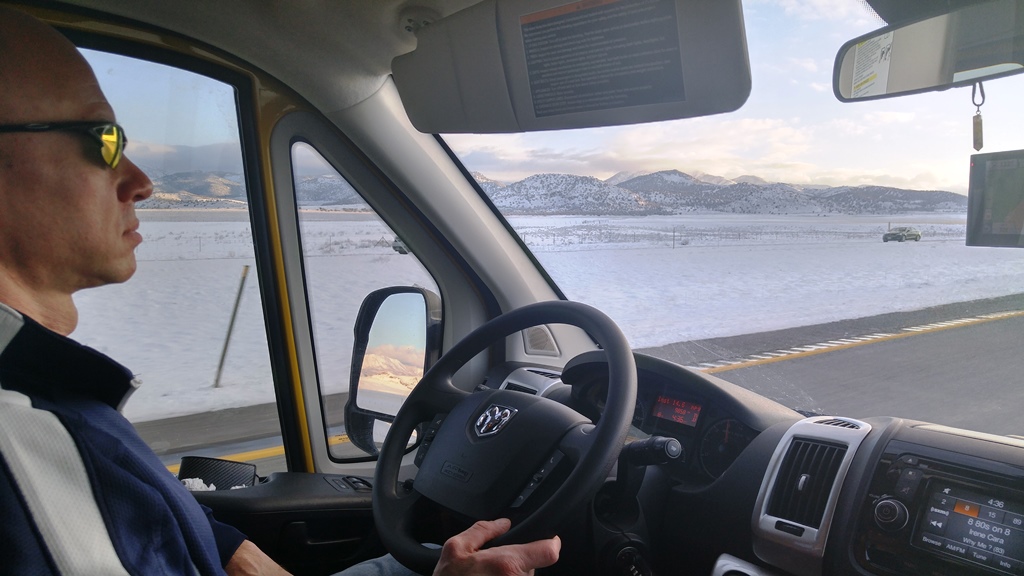 James driving Winnebago Travato on road with snowy surroundings.