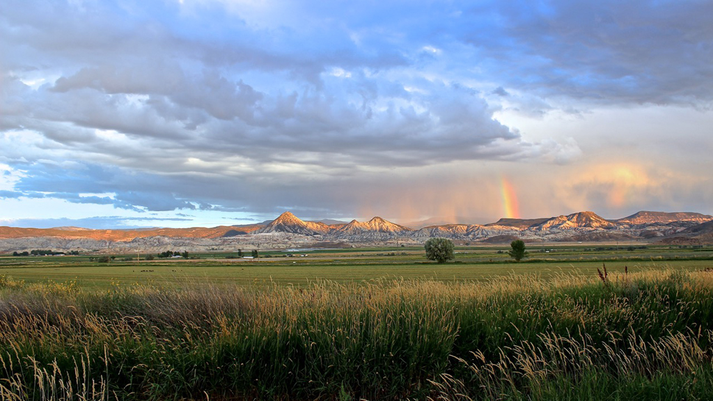 Grassy field with mountains ahead and a rainbow over the mountains.