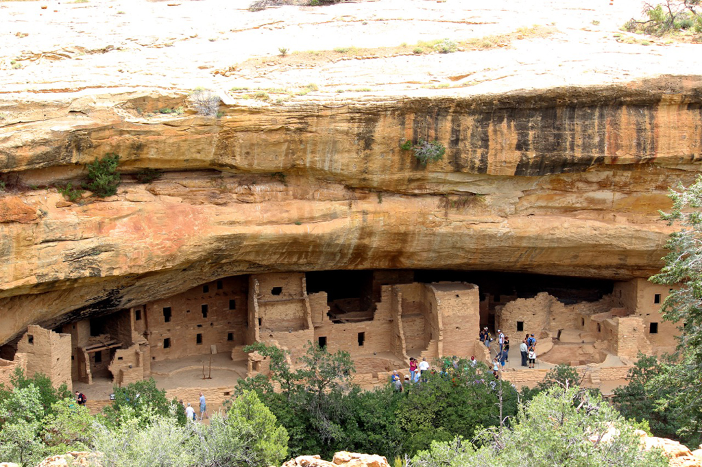 Crowds exploring ancient stone homes built into side of a cliff.