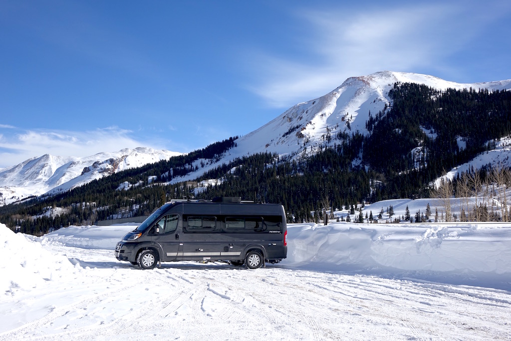 Winnebago Travato in snow covered parking lot with mountains in the background.