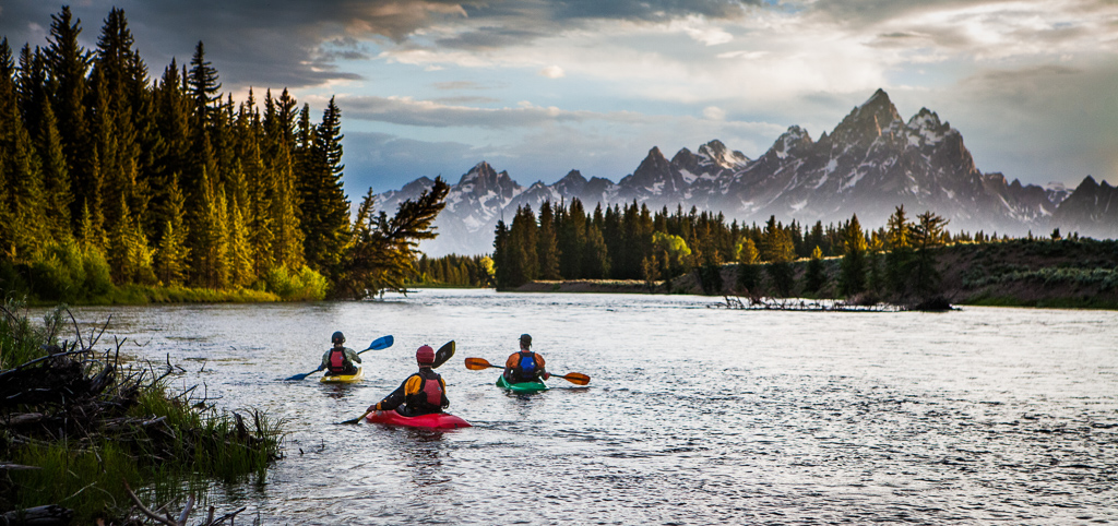 3 kayakers in the water with the Grand Tetons in the distance.