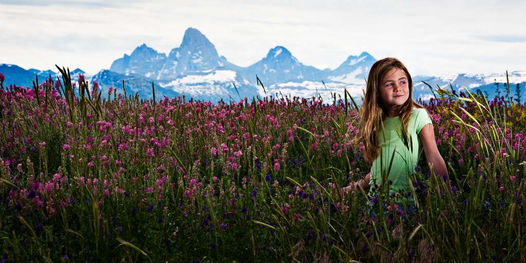 Child sitting in field of flowers with mountains in the background.