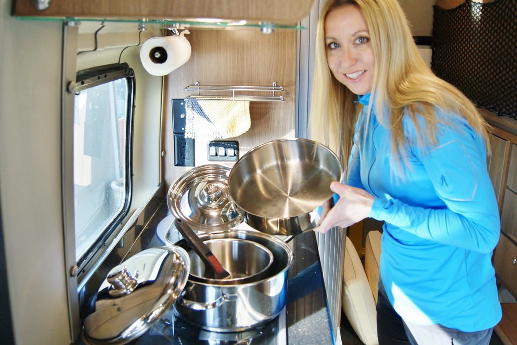 Stef showing Magma cookware set while standing in kitchen of Winnebago Travato.