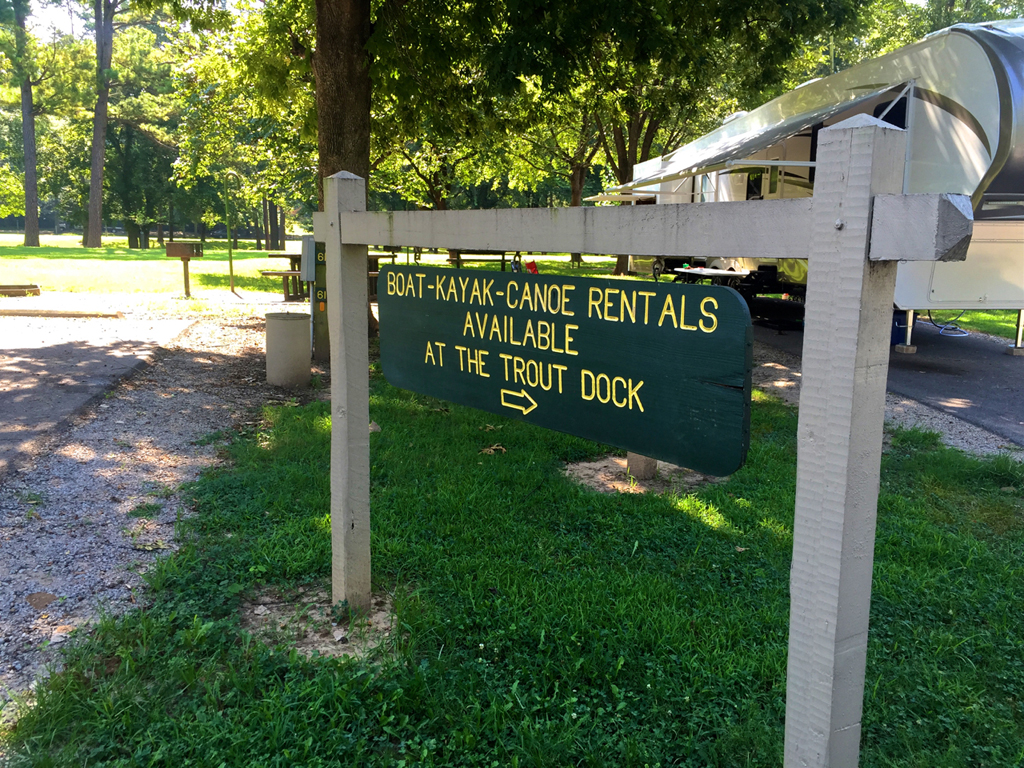 Sign at a campground with arrow that says, "Boat-Kayak-Canoe Rentals Available at the Trout Dock."