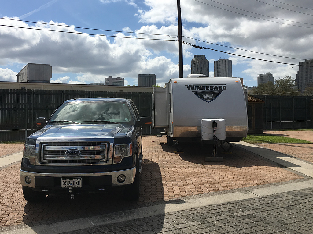 Truck parked next to a Winnebago towable with tall buildings of downtown New Orleans in the background.