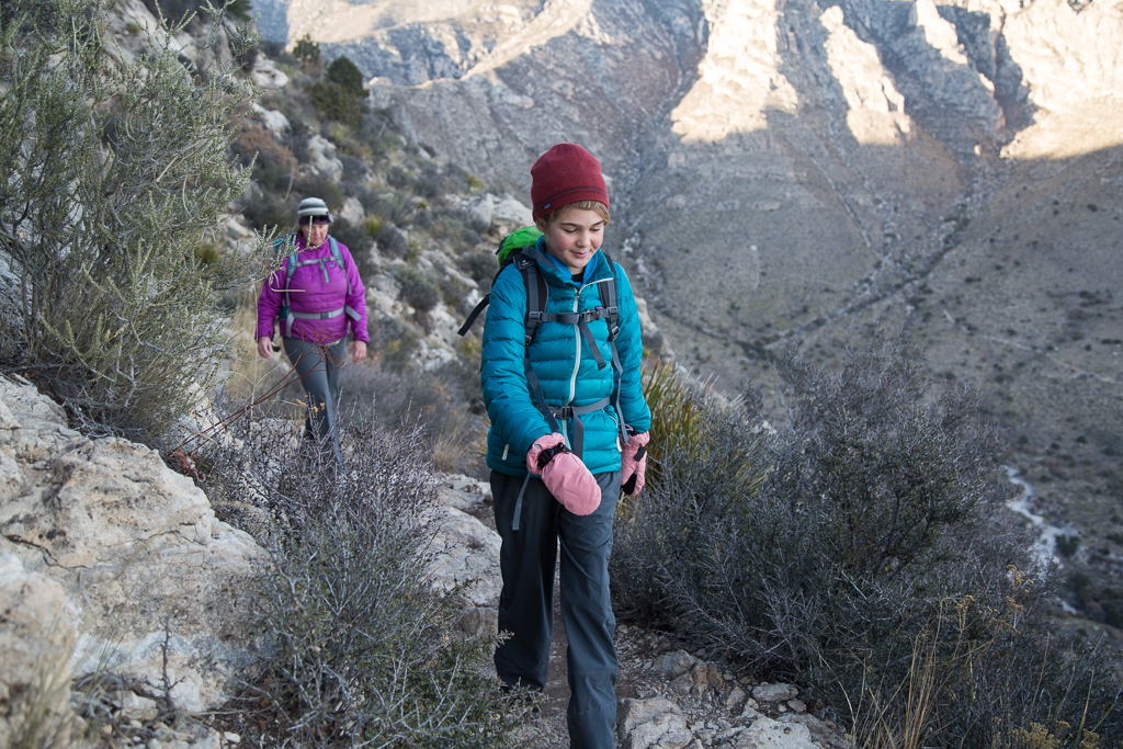 Abby and Kathy walking along a narrow rocky hiking trail along the side of the mountains.