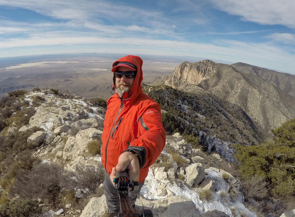 Peter taking a selfie at the peak of the mountain range with view of the mountain range behind and ground below.