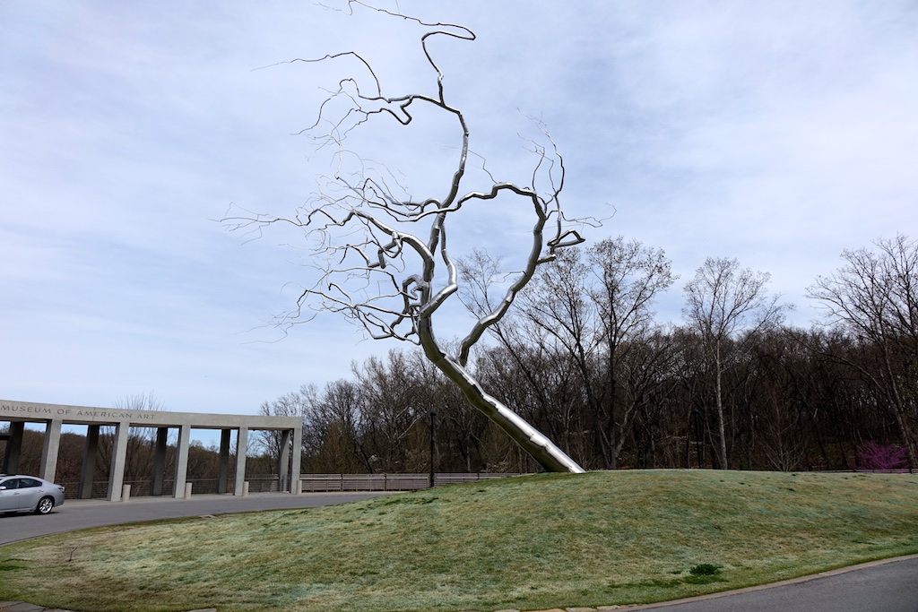 Silver tree sculpture on grass at the museum entrance.