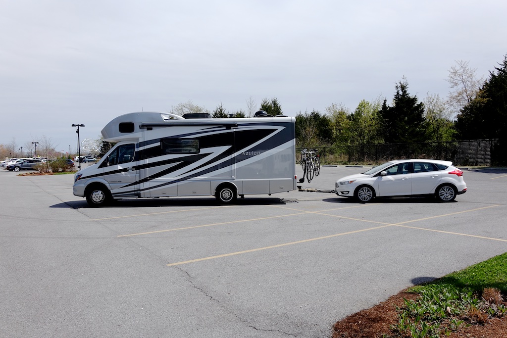 Winnebago Navion with Ford Focus tow car attached parked in a parking lot.