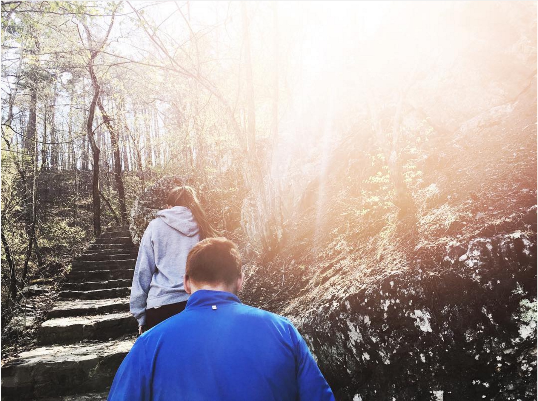 Man and Woman hiking up steps on the side of a hill with sunlight beaming down.
