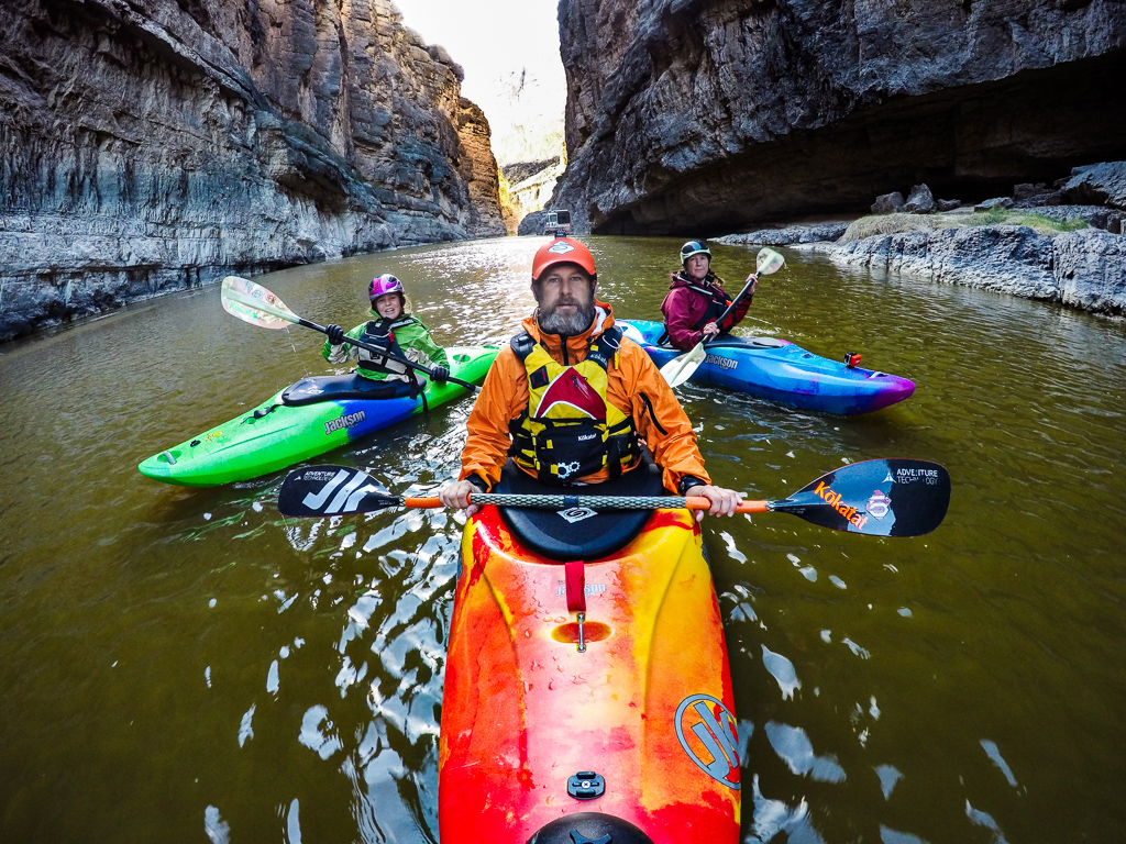 Peter, Kathy, and Abby in kayaks on the river with the canyon walls rising high on either side of them..