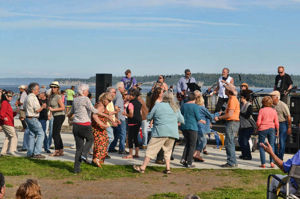 Crowd dancing to a band playing music at the water edge.