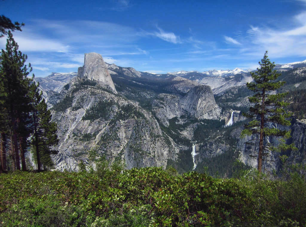 View over the trees of half dome and the mountains, river, waterfall and valleys surrounding.