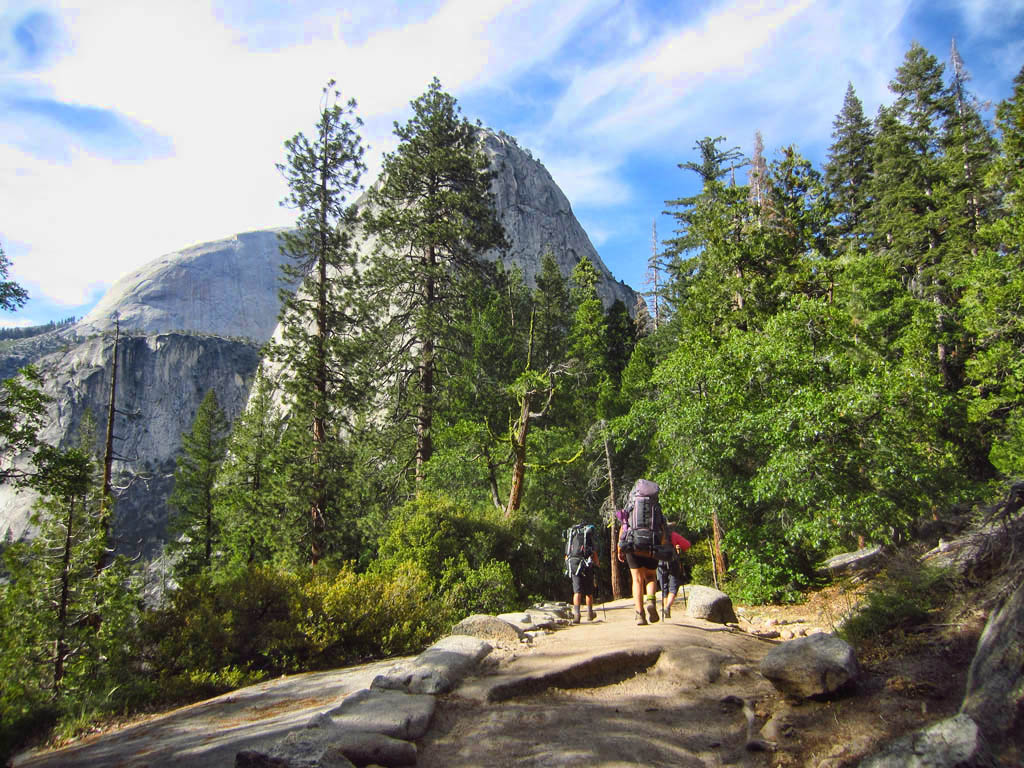 Hikers on a trail that leads through the trees to Half Dome.