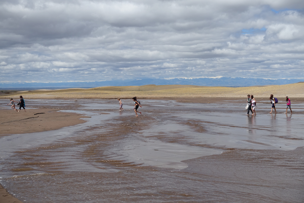People walking across Crossing Medano Creek that runs through the middle of the sand dunes.