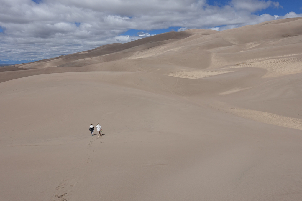 Two people walking across sand dunes.