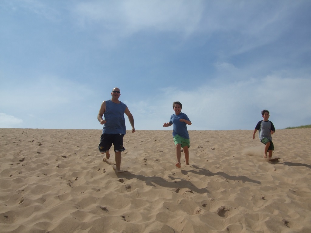 Man and two boys running down a sand dune.