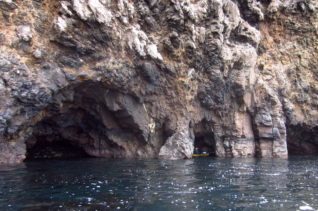 Kayaker at the start of a cave alongside the cliff.
