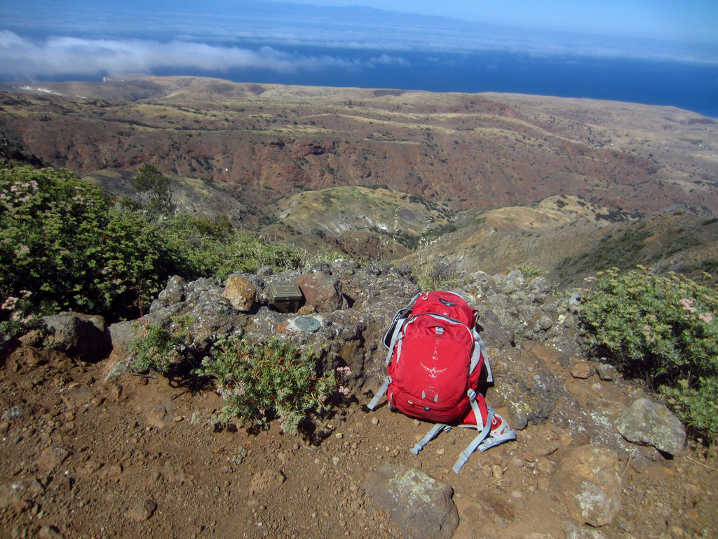 Red backpack sitting on rocky hillside overlooking hills leading to the water.