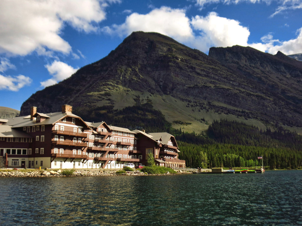Large hotel on the water at the base of mountains.