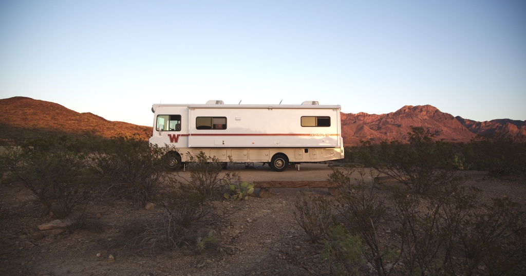 Winnebago Brave parked in desert landscape with red rocky dunes in the background.