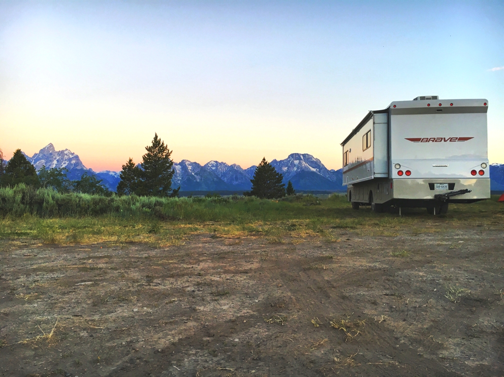 Winnebago Brave in grassy field with Tetons in the distance.