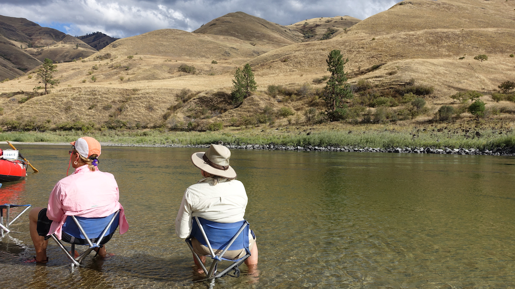 People sitting in camping chairs in the shallow of the river.