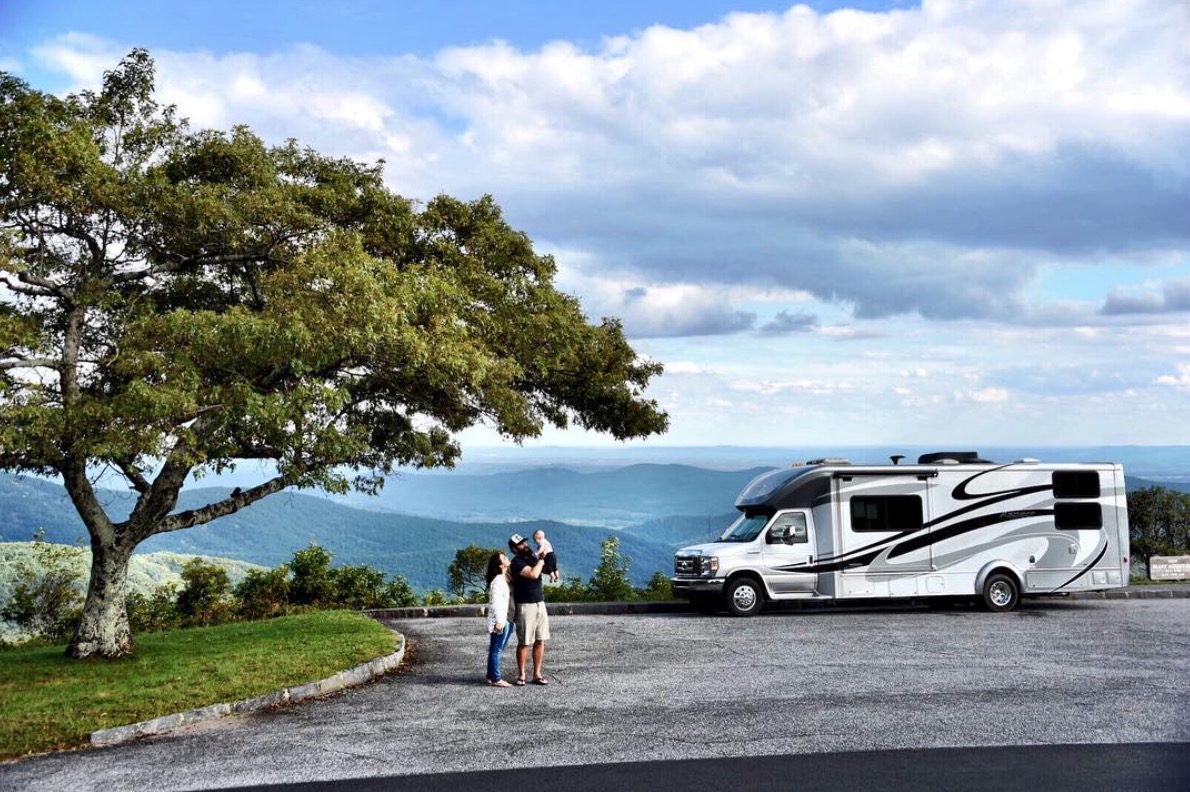 Couple holding baby in the air smiling standing outside their motorhome.