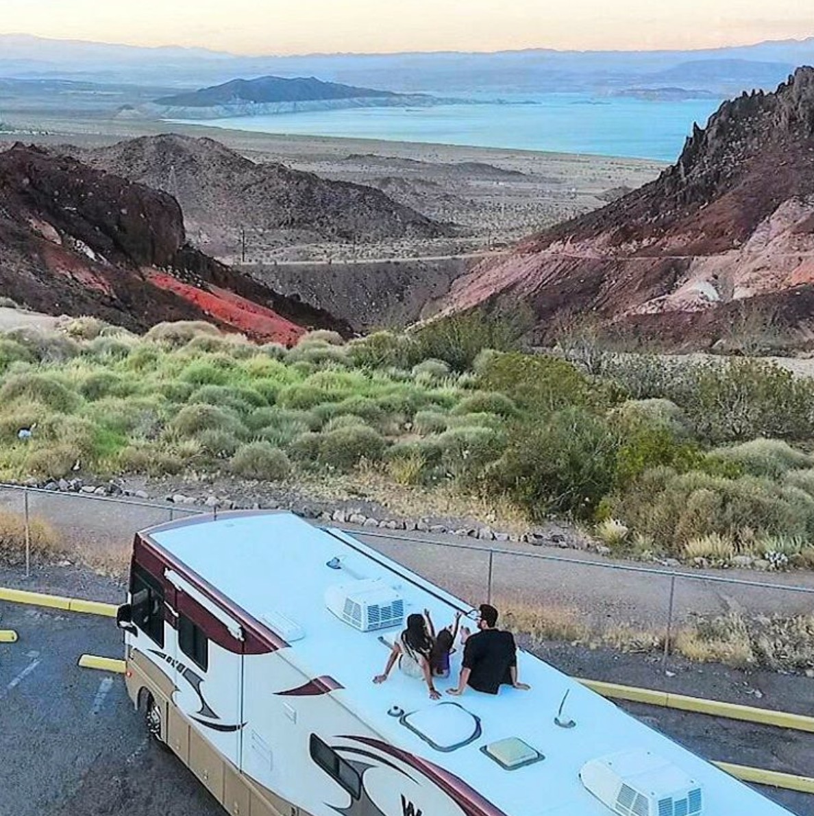 Couple sitting on their motorhome looking out over landscape and water ahead.