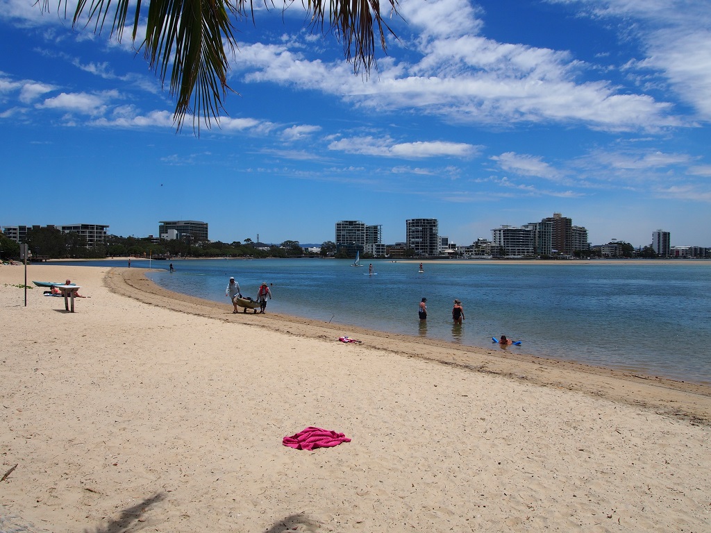 People on the beach and in the water at Cotton Tree Beach with resorts on the far side of the beach.