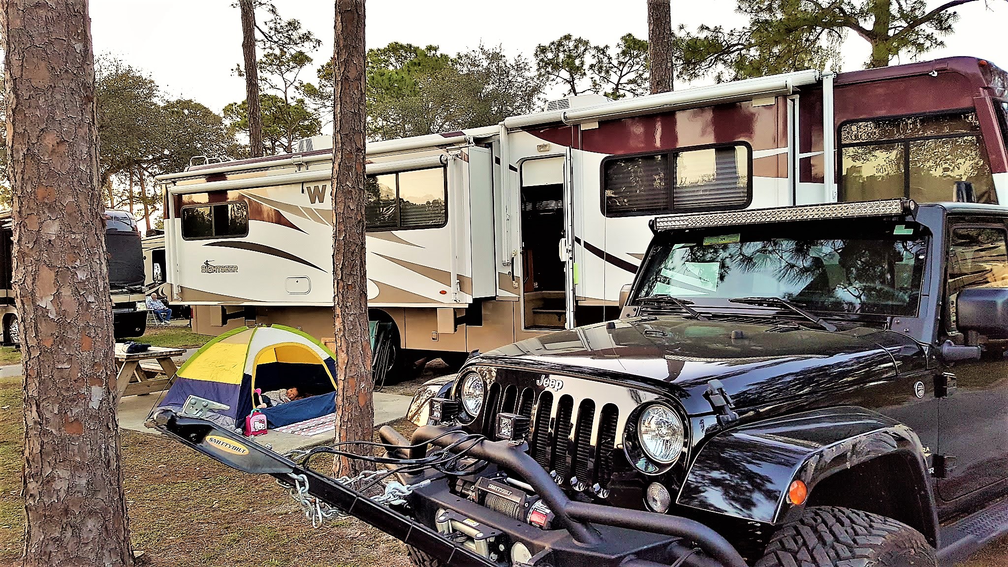 Winnebago Sightseer in campground with small tent and a jeep out front.