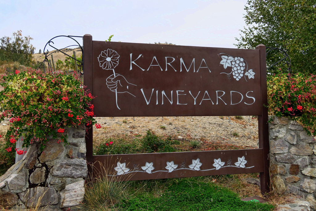 Sign for Karma Vineyards with flowers on either side.