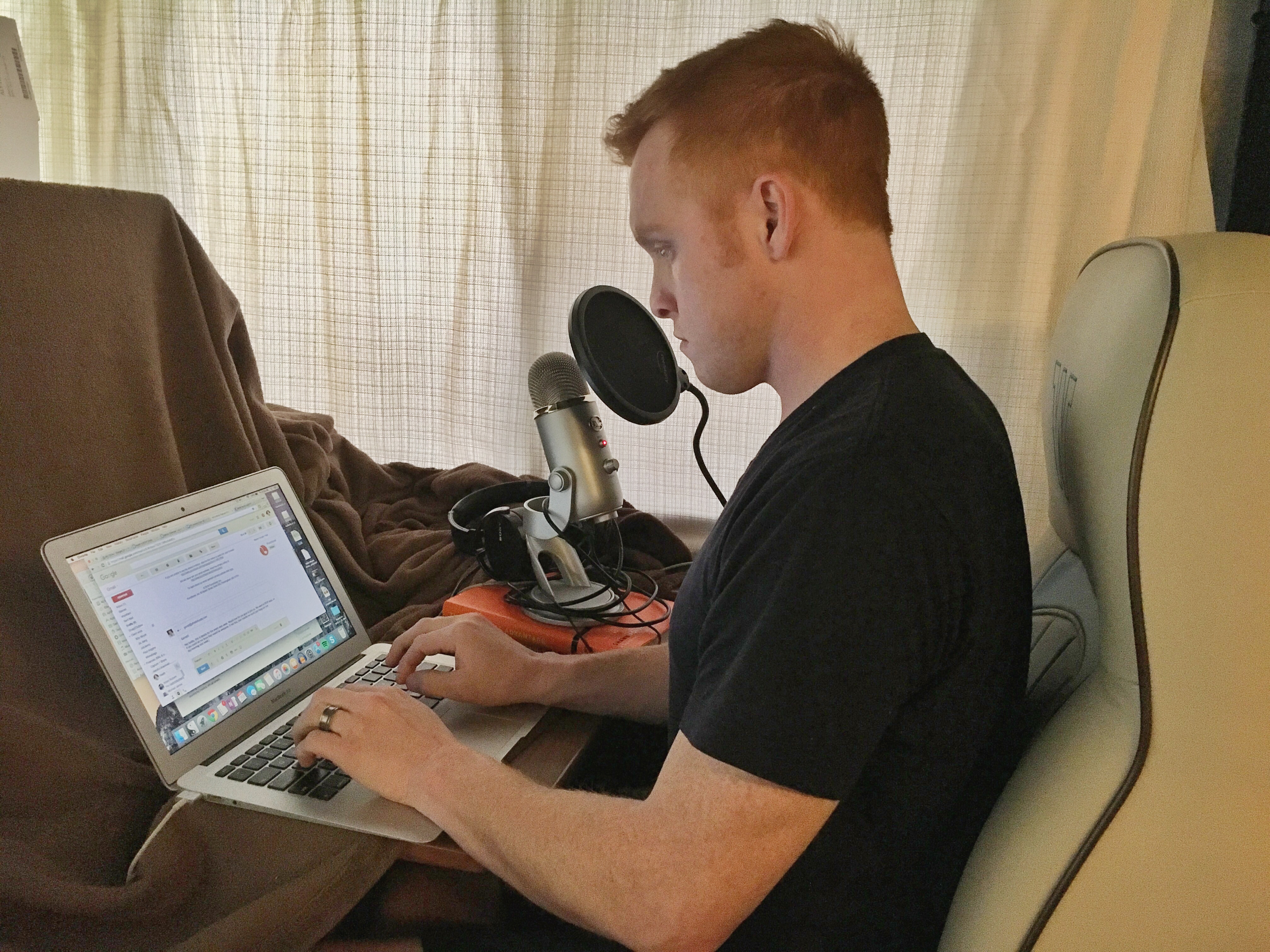 Heath working on laptop with podcast equipment next to him. 