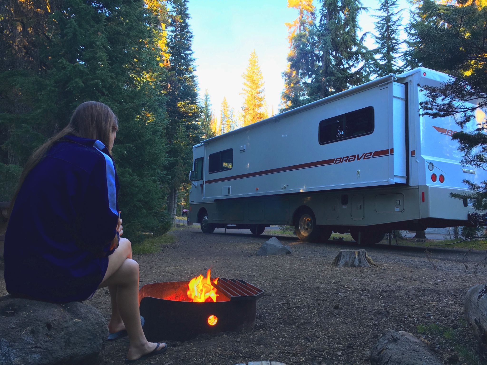 Alyssa sitting by a campfire outside their parked Winnebago Brave.