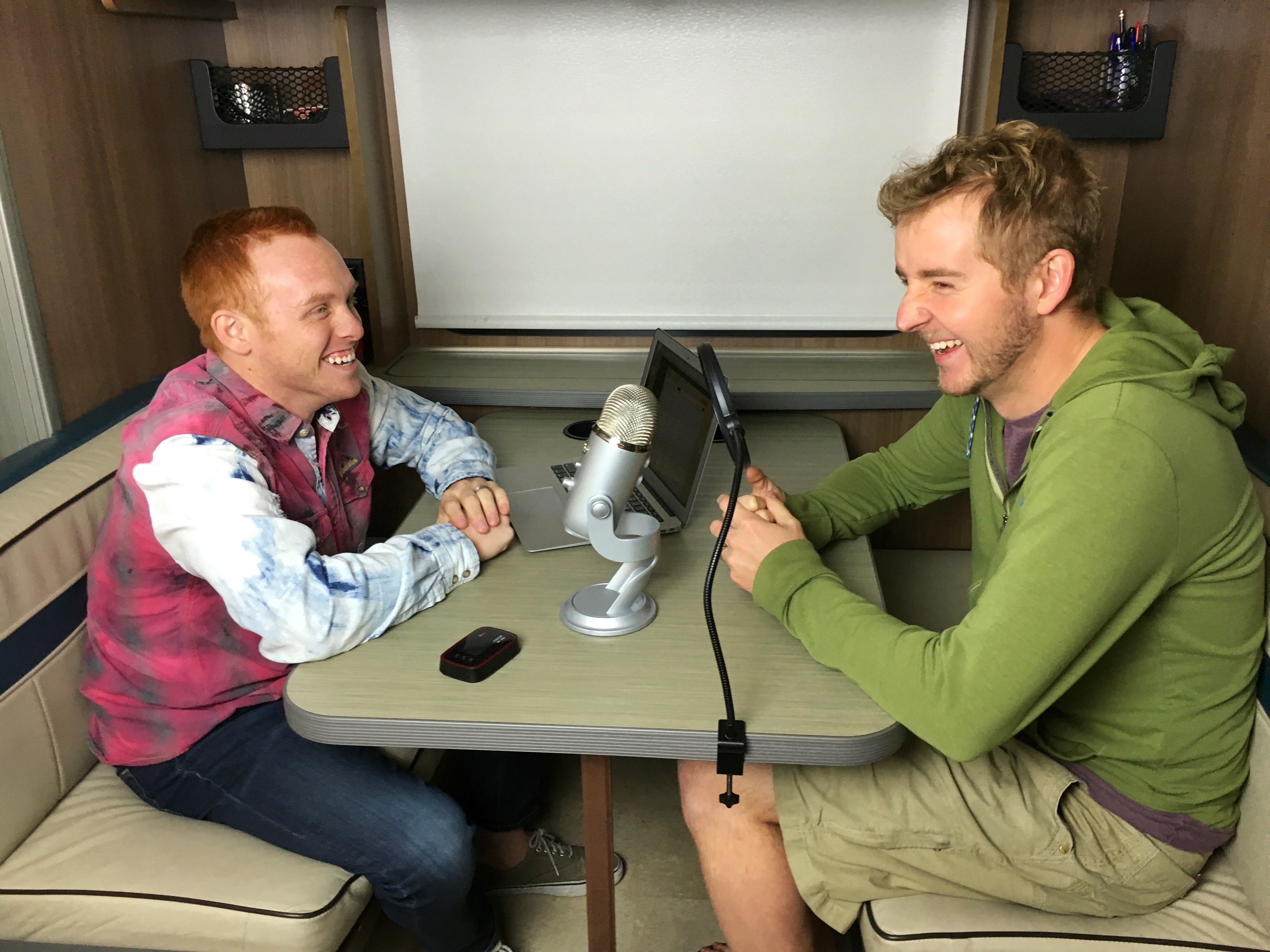 Two men sitting at motorhome dinette recording a podcast.