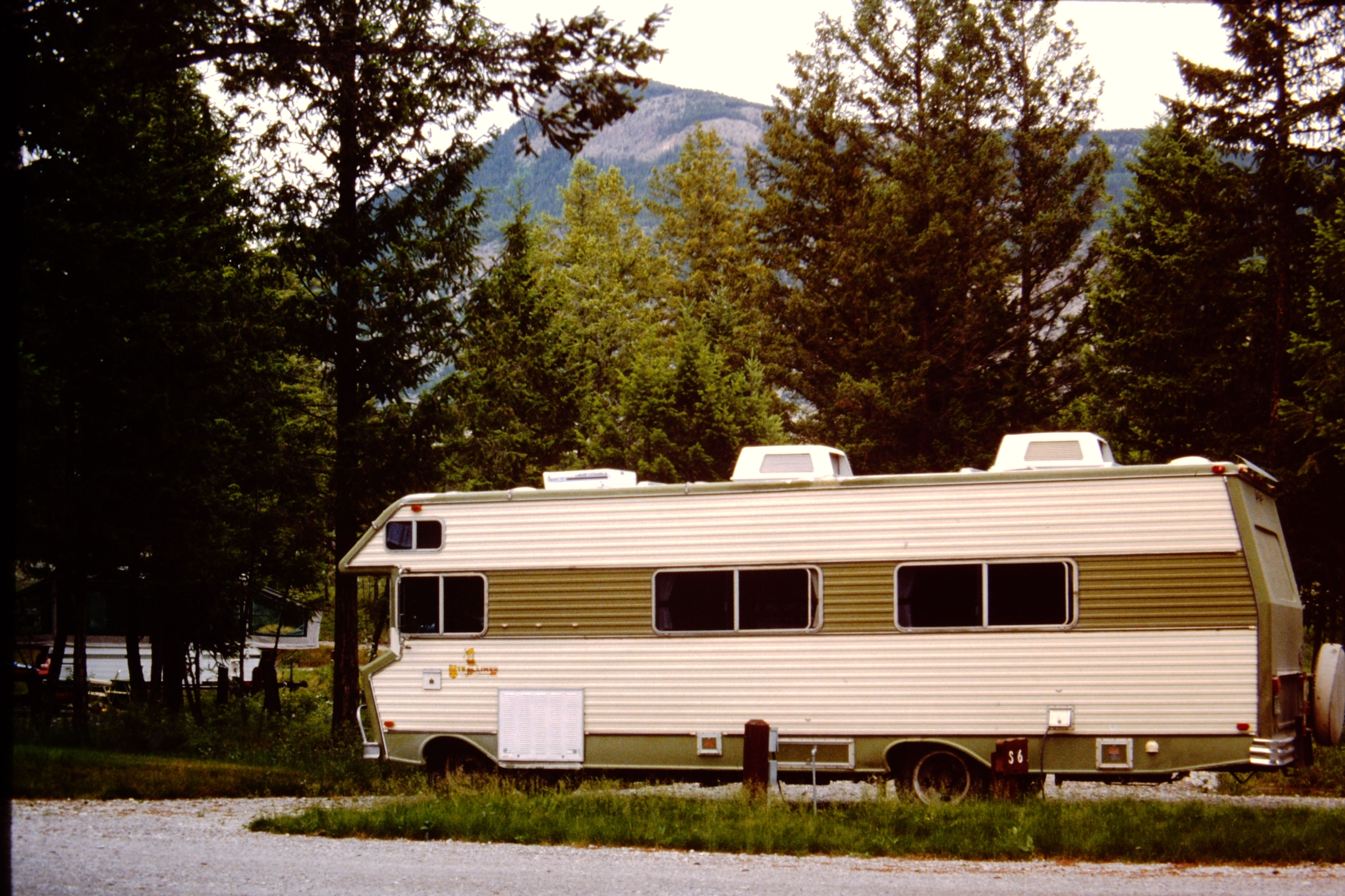 Old motorhome parked in campsite with mountains in the distance.
