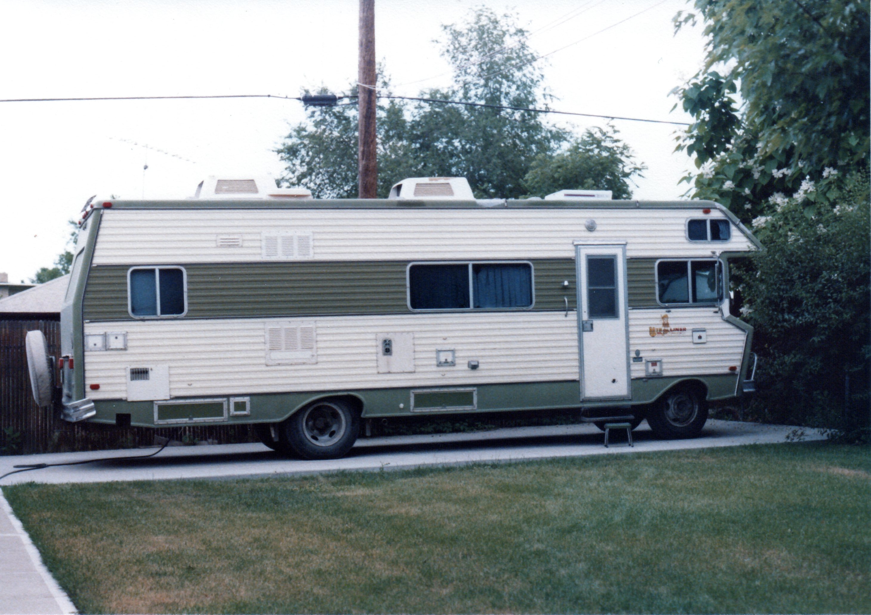 Old motorhome on paved parking pad outside house.