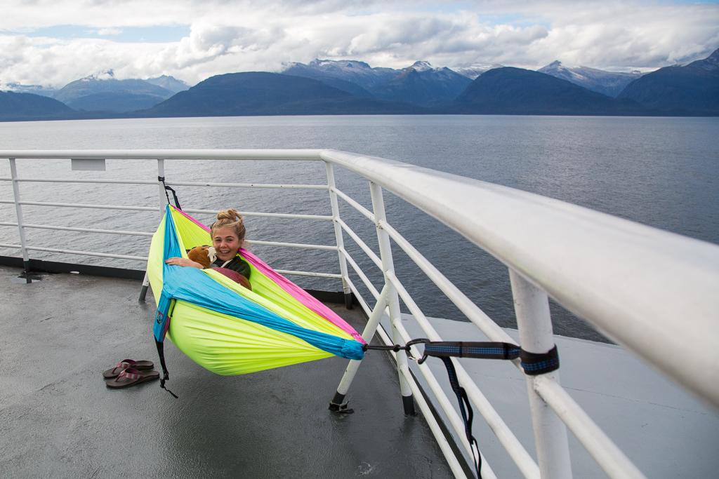 Abby in a hammock at the front of the boat with mountains ahead.