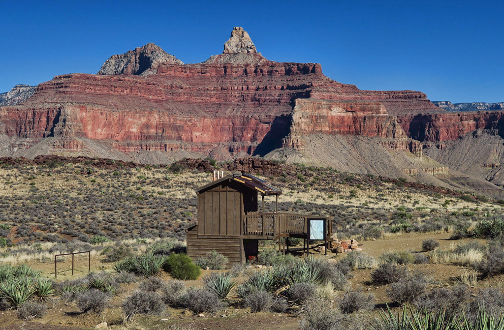 Wooden building in desert landscape with rocky canyon ahead.