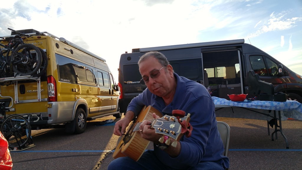 Man playing a guitar in front of two Winnebago Travatos