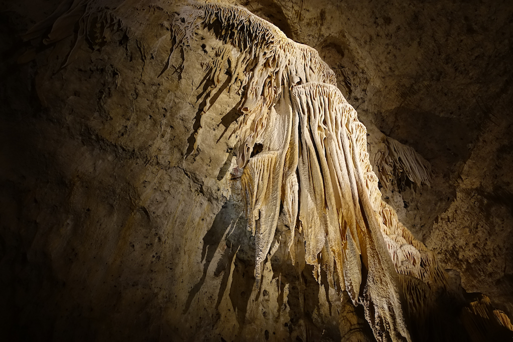 Incredible formations of stalactites going down a side of the cavern lit up by lights.