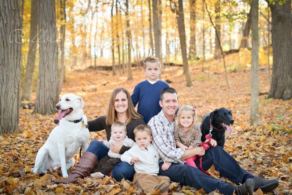 Family of 6 and two dogs sitting among fallen leaves of Fall.