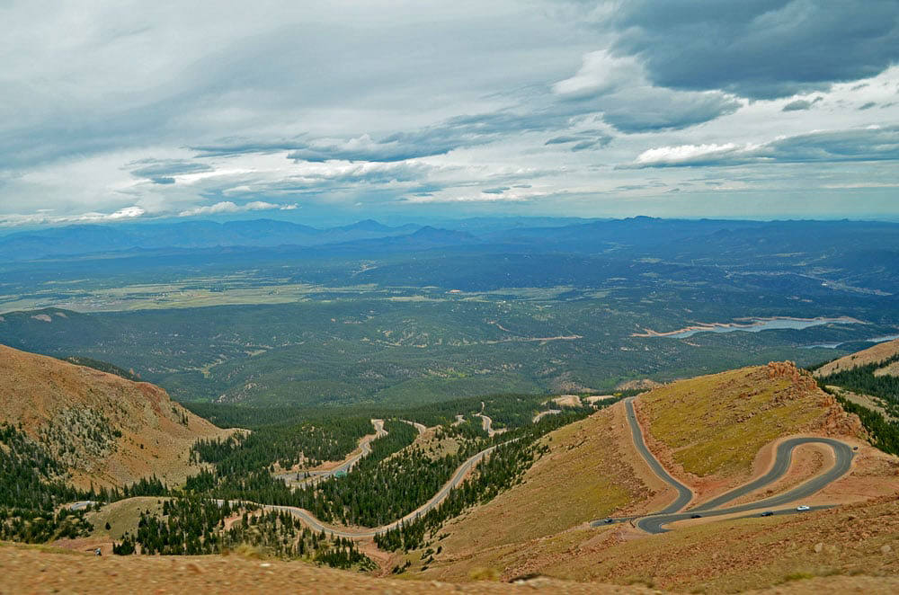 Narrow winding road up the side of the mountain to Pikes Peak with mountains in the distance.