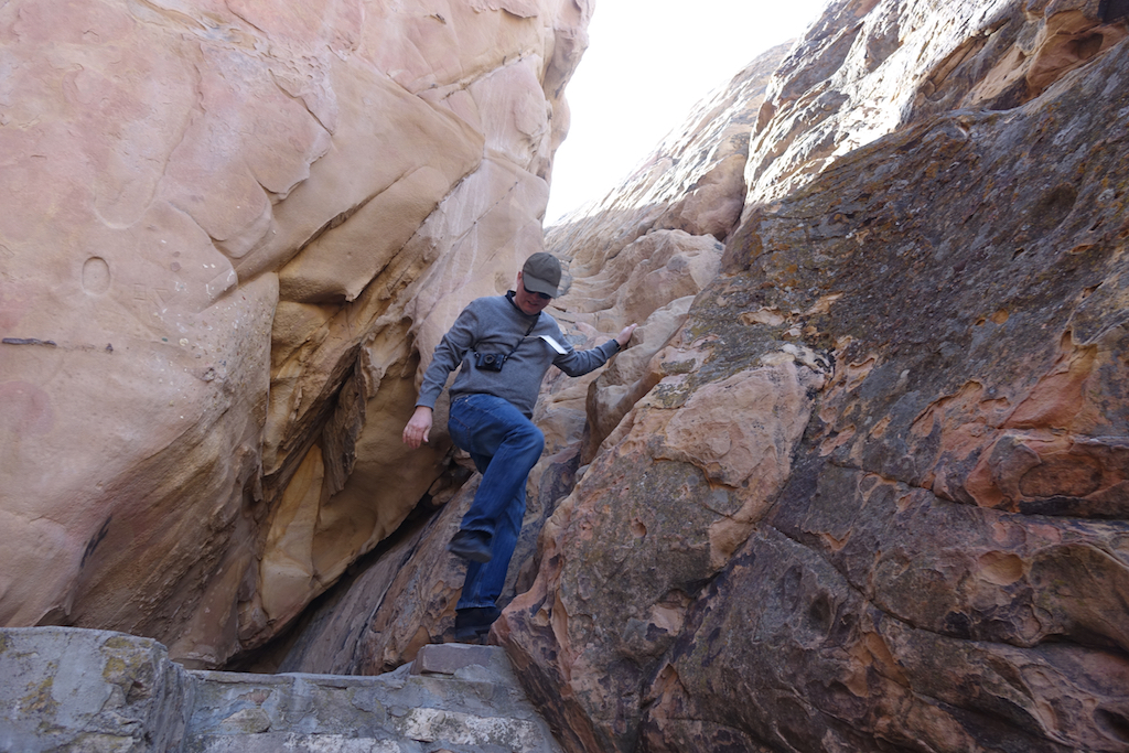 Man descending down narrow path between two large boulders.