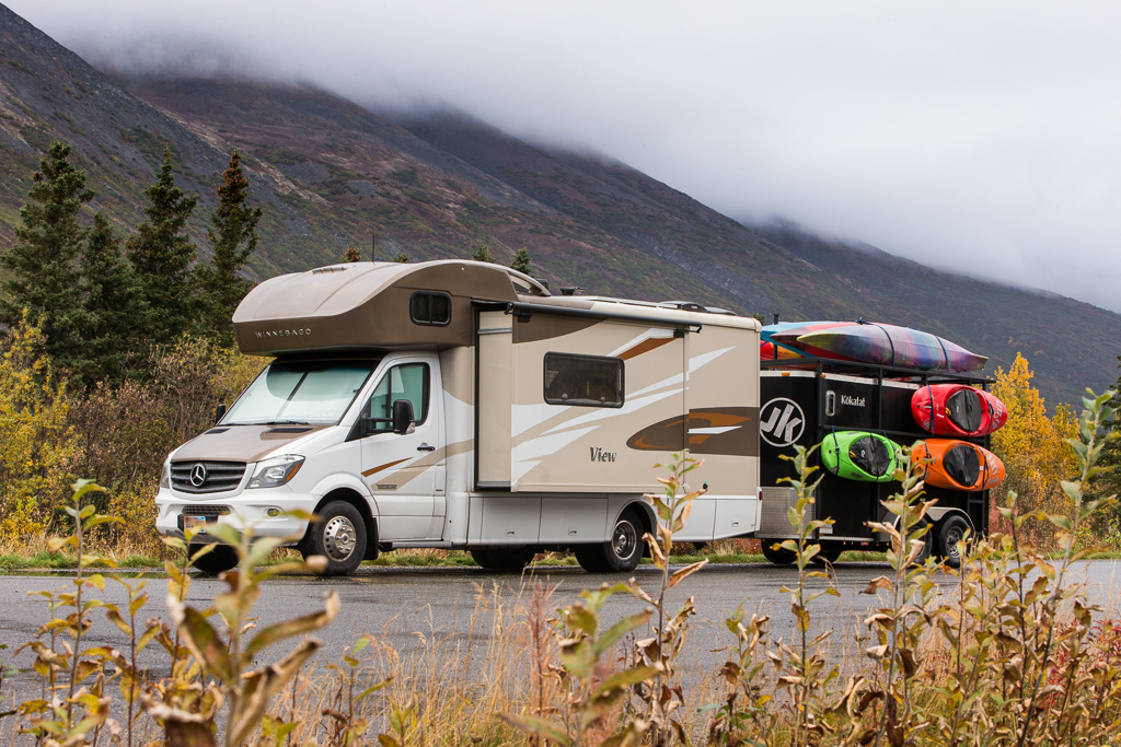 Winnebago View with trailer attached parked alongside fog-covered mountains.
