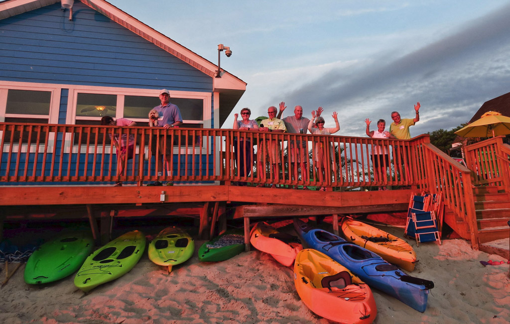 Group of people waving from deck of home on the beach.
