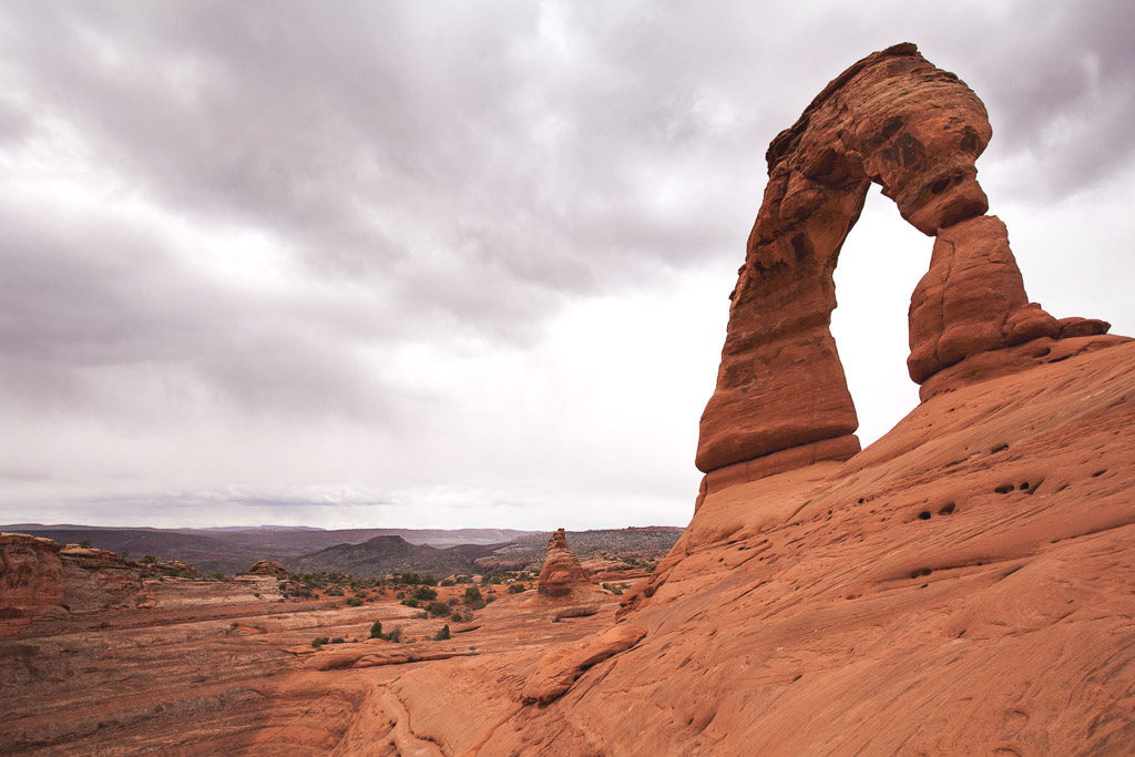 Red rock arch at Arches National Park with rocky landscape fading to green landscape in the distance.