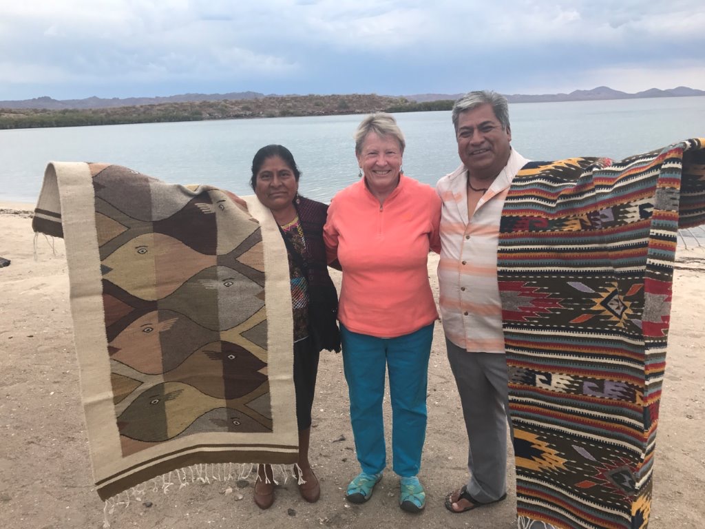 Woman next to people holding beautifully crafted blankets.